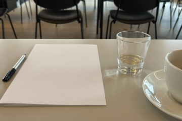 Vorbereiteter Arbeitsplatz mit Block, Wasser und Kaffee in einem Seminarraum