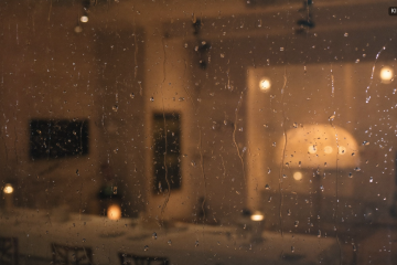 Regentropfen am Fenster vor einem warm beleuchteten Festsaal als Plan B bei schlechtem Wetter