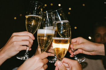 Anstoßen mit Sektgläsern zu Silvester vor goldenen Lichtern und Konfetti
